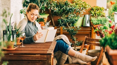 Eine Frau sitzt auf einem Balkon mit Pflanzen und liest. Pflanzen und Wildblumen auf dem Balkon helfen Insekten beim Überleben. | Bild: colourbox.com