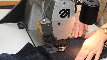 Frau näht an Nähmaschine eine Hose. Was bedeuten Sprichwörter mit Alltagsgegenständen wie Fäden, Gardinen und Senf? Wir plaudern aus dem Nähkästchen, was Redensarten und Redewendungen bedeuten.  | Bild: picture-alliance/dpa