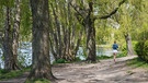 Eine Joggerin läuft an der Außenalster in Hamburg. Mehr als 20 Millionen Menschen in Deutschland laufen, um fit zu bleiben. Wie wurden wir eigentlich zu solch begeisterten Joggern? Wann wurde das Laufen erfunden und von einer Art Beruf zum Hobby? Wir blicken auf die Geschichte des beliebten Sports. | Bild: picture alliance/dpa | Marcus Brandt