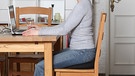 Richtig sitzen für einen gesunden Rücken: So wie im Bild (mit Sitzkissen) funktioniert' s ... Langes Sitzen kann schnell zu Rückenproblemen und Schmerzen führen. Doch es gibt einige Möglichkeiten, es dem Rücken angenehmer zu machen. | Bild: BR