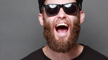 Ein Hipster mit Bart, Sonnenbrille und Tattoo. Haben sich Bärte in der Menschheit entwickelt, um vor Faustschlägen ins Gesicht zu schützen? Für die Überprüfung dieser steilen These gab es 2021 den Friedens-Ig-Nobelpreis. | Bild: stock.adobe.com/4Max