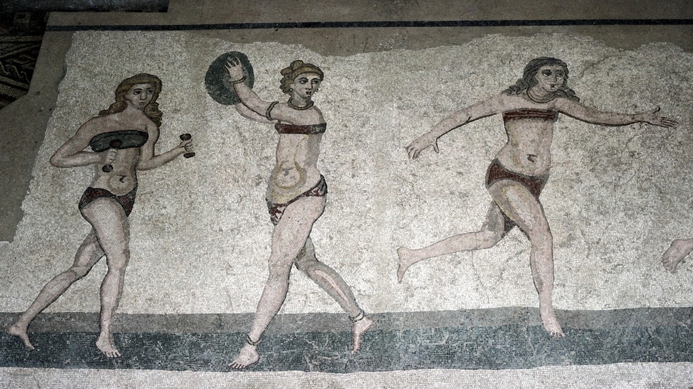 Ein römisches Mosaik aus dem 4. Jahrhundert. n. Chr. zeigt die sogenannten "Bikinimädchen" in der Villa Romana del Casale, Sizilien. Viele Menschen treibt die Angst um, in ihrer Freizeit etwas zu verpassen. Wir haben Tipps gegen FOMO und Freizeitstress, damit ihr euch in eurer freien Zeit wirklich erholt. | Bild: picture alliance / Artcolor Ein römisches Mosaik aus dem 4. Jahrhundert. n. Chr. zeigt die sogenannten "Bikinimädchen" in der Villa Romana del Casale, Sizilien. Viele Menschen treibt die Angst um, in ihrer Freizeit etwas zu verpassen. Wir haben Tipps gegen FOMO und Freizeitstress, damit ihr euch in eurer freien Zeit wirklich erholt. | Bild: picture alliance / Artcolor