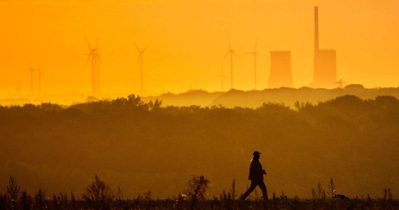 Ein Mann geht über einen Feldweg, während am Horizont das Kohlekraftwerk Mehrum zu sehen ist. | Bild: picture alliance/dpa | Julian Stratenschulte Ein Mann geht über einen Feldweg, während am Horizont das Kohlekraftwerk Mehrum zu sehen ist. | Bild: picture alliance/dpa | Julian Stratenschulte