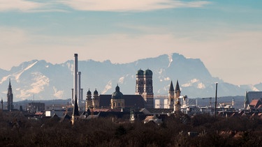 Die Skyline der bayerischen Landeshauptstadt ist bei Föhnwetter vor der Kulisse der etwa 90 Kilometer entfernten Alpen mit der Zugspitze (rechte Bildhälfte hinter der Frauenkirche) zu sehen. Der Föhn ist ein Fallwind, der in den Bergen der Alpen entsteht und für warme Luft sorgt. Bei Föhn herrscht oft mildes, sonniges Wetter. Umstritten ist, ob der Föhn für Wetterfühligkeit wie Kopfschmerzen verantwortlich ist. | Bild: picture alliance/dpa | Peter Kneffel