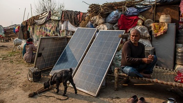 Solarpanäle im ländlichen Gebiet von Neu Delhi in Indien erzeugen Sonnenergie. Im Hintergrund einfache Hütten als Übergangslösung, da weite Teile überflutet wurden. Die Ungleichheit wird weiter wachsen und die Armen noch ärmer werden, wenn wir nicht bald etwas tun - so der Club of Rome in seinem Bericht von September 2022. | Bild: picture alliance / ZUMAPRESS.com | Pradeep Gaur