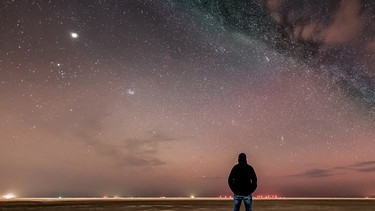 Der Sternenhimmel über der Insel Borkum mit Blick nach Nordwesten, mit der Milchstraße und einer Sternschnuppe, fotografiert am 22. März 2025 von Thomas Sauer. In der linken Bildhälfte ist der große und helle Planet Jupiter zu sehen, rechts unter ihm der Offene Sternhaufen der Plejaden im Sternbild Stier. | Bild: Thomas Sauer